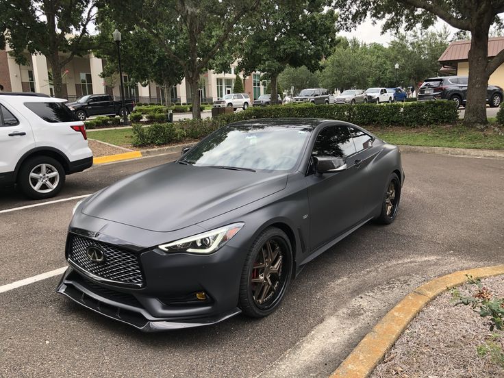 a gray sports car parked in a parking lot next to some trees and cars on the street