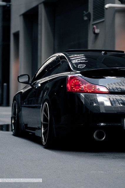 a black car parked on the street in front of a building with its lights on