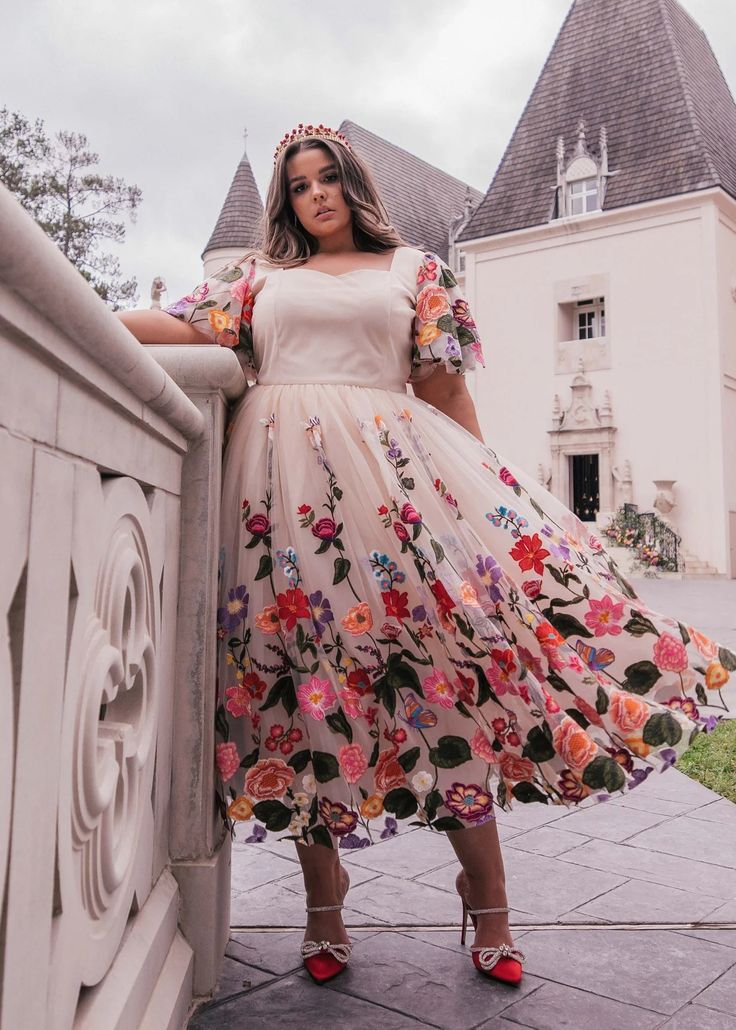 a woman in a floral dress leaning against a wall with her hands on her hips