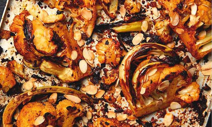 roasted vegetables with almonds and seasoning in a baking dish on a table top