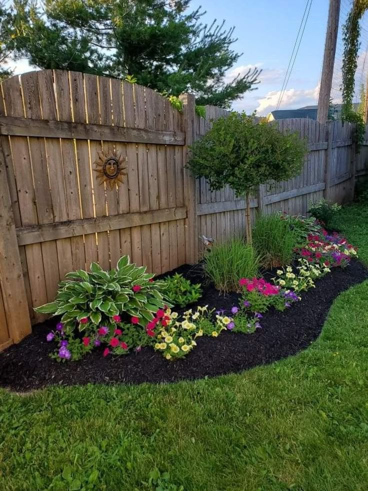 a garden area with flowers and plants in the grass next to a wooden privacy fence