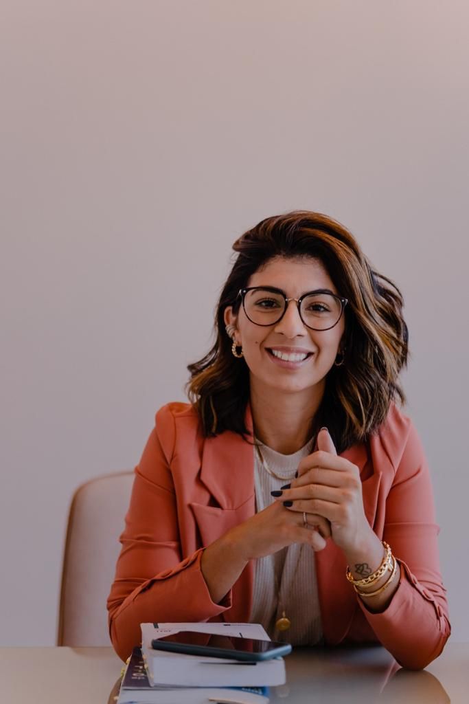 a woman sitting at a table with books in front of her and smiling for the camera