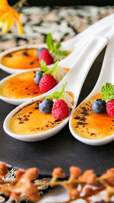 four dessert spoons with fruit on them sitting on a table next to other food items