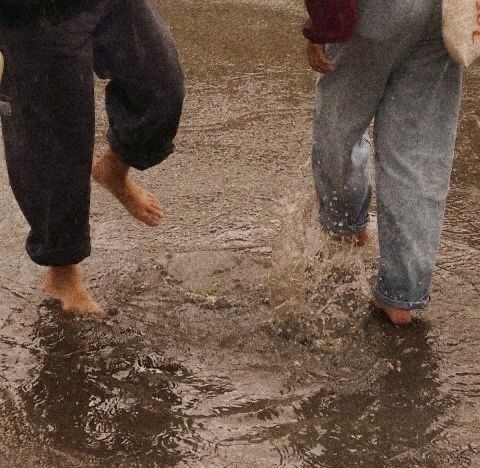 two people are walking in the rain with their feet up and one person is holding an umbrella