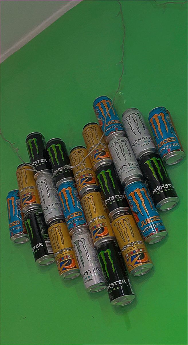 six cans of monster energy drink on a green surface