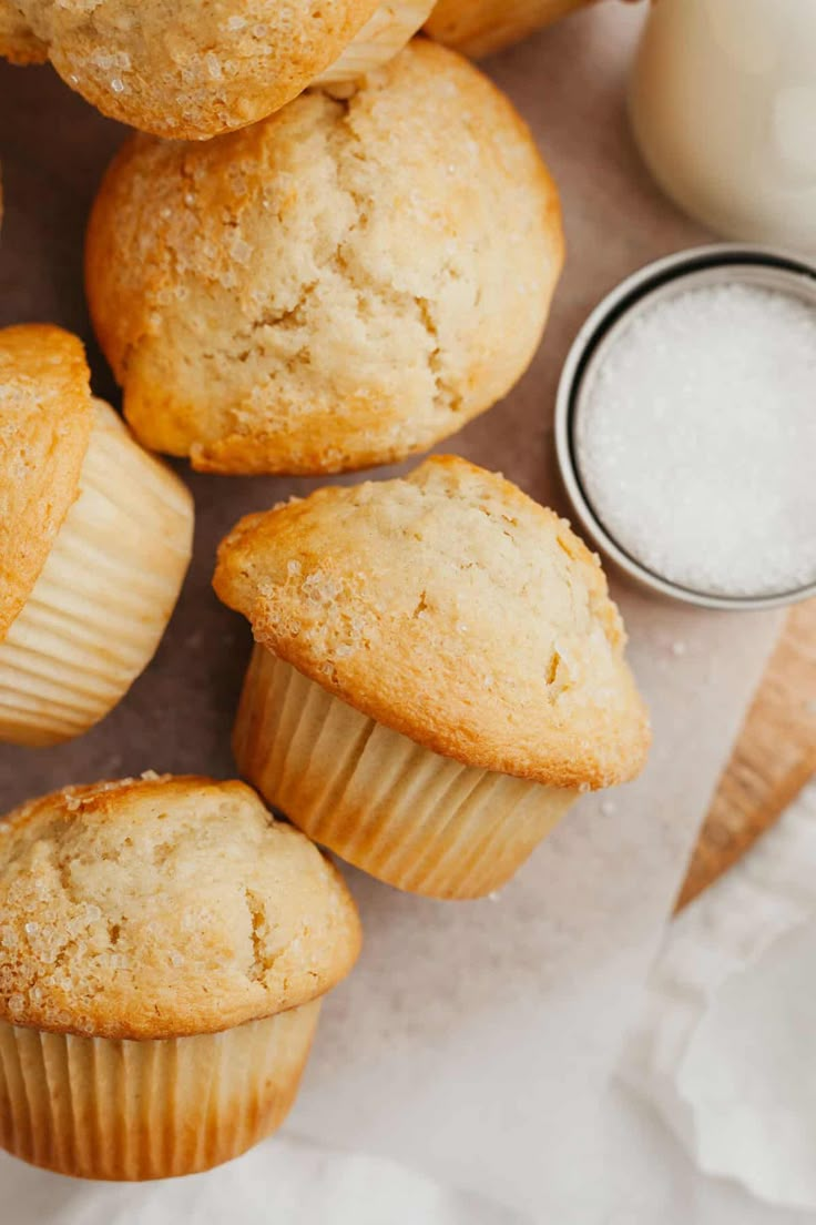 several muffins on a table next to a bottle of milk and some sugar