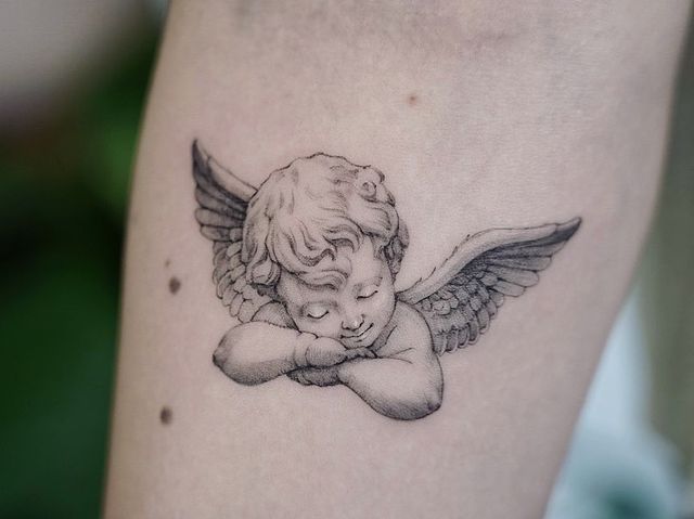 an angel tattoo on the leg of a woman with her head tucked under her arm