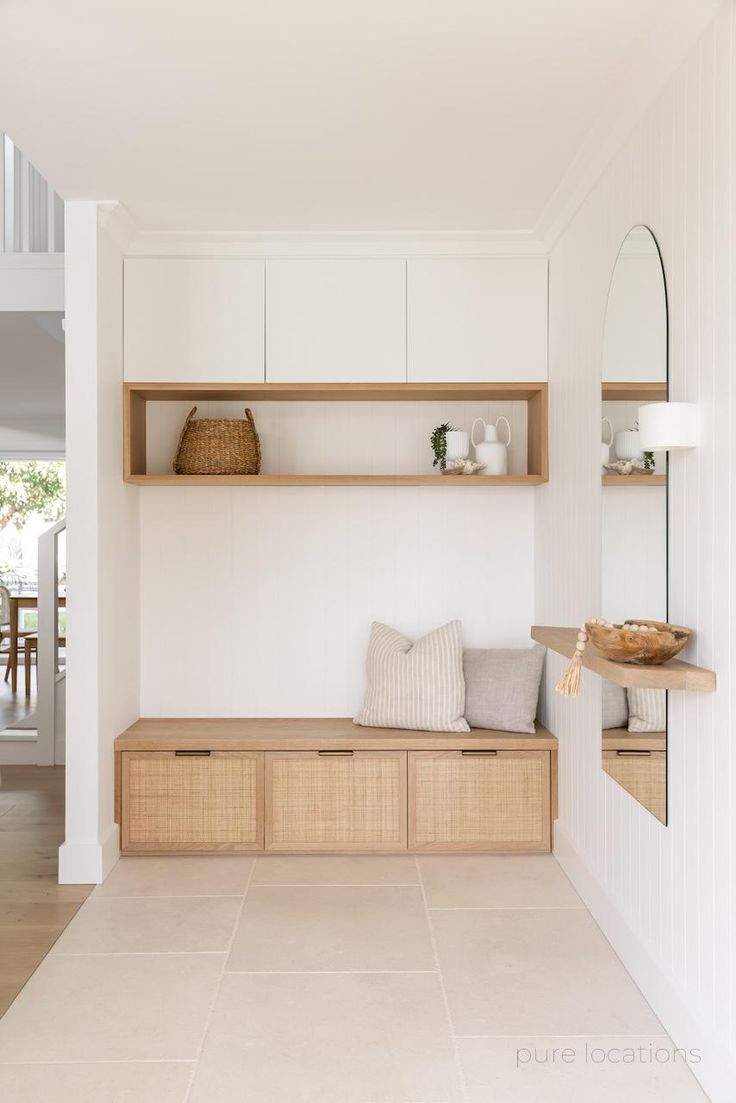 a wooden bench sitting under a mirror on top of a white wall next to a shelf