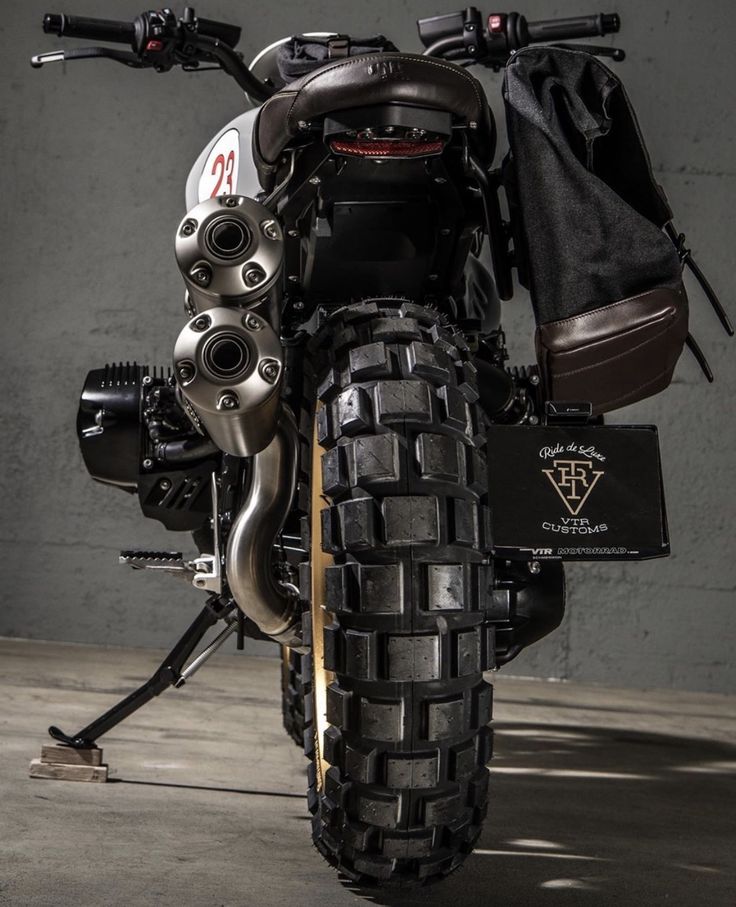 the back end of a motorcycle parked in front of a wall with a bag on it