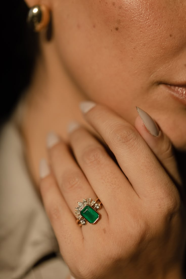 a close up of a person wearing a ring with a green stone on it's finger