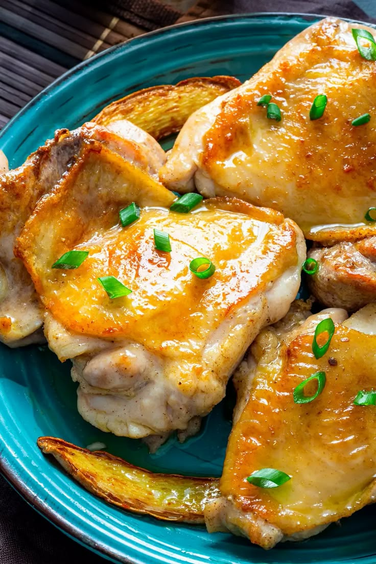 a blue plate topped with chicken covered in sauce and garnished with green onions