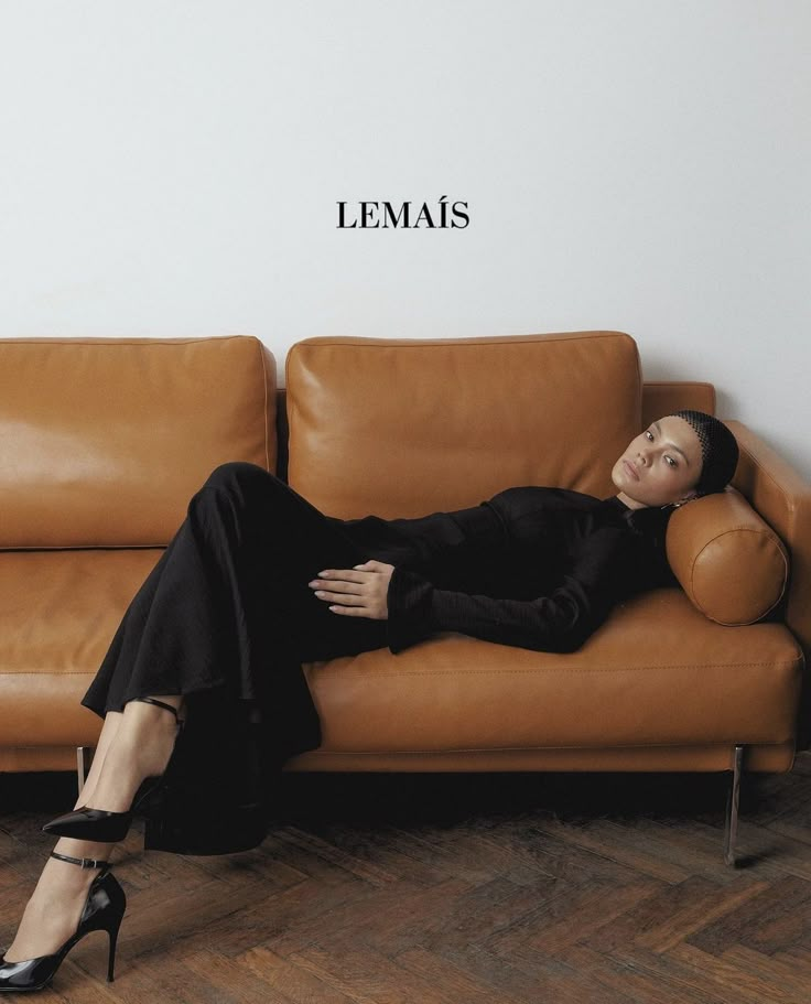 a woman laying on top of a brown leather couch next to a wall with the word lemais