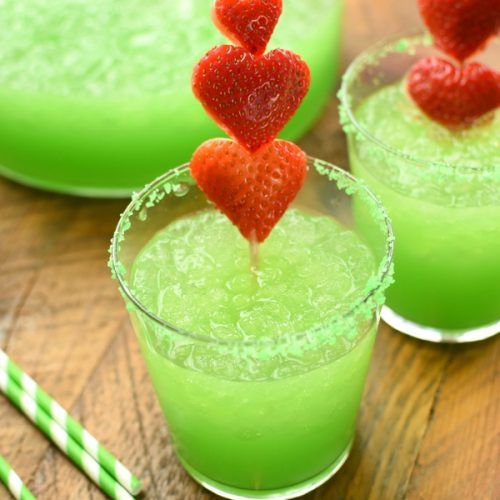 two glasses filled with green liquid and strawberries on the top one has red heart shaped strawberries