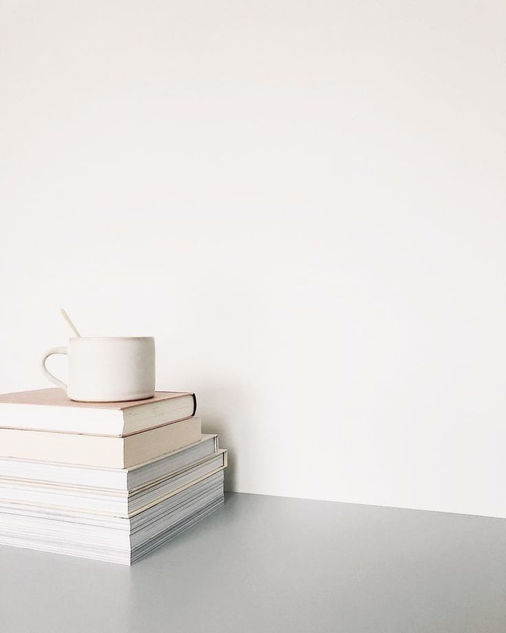 a stack of books with a coffee cup on top of it next to a white wall