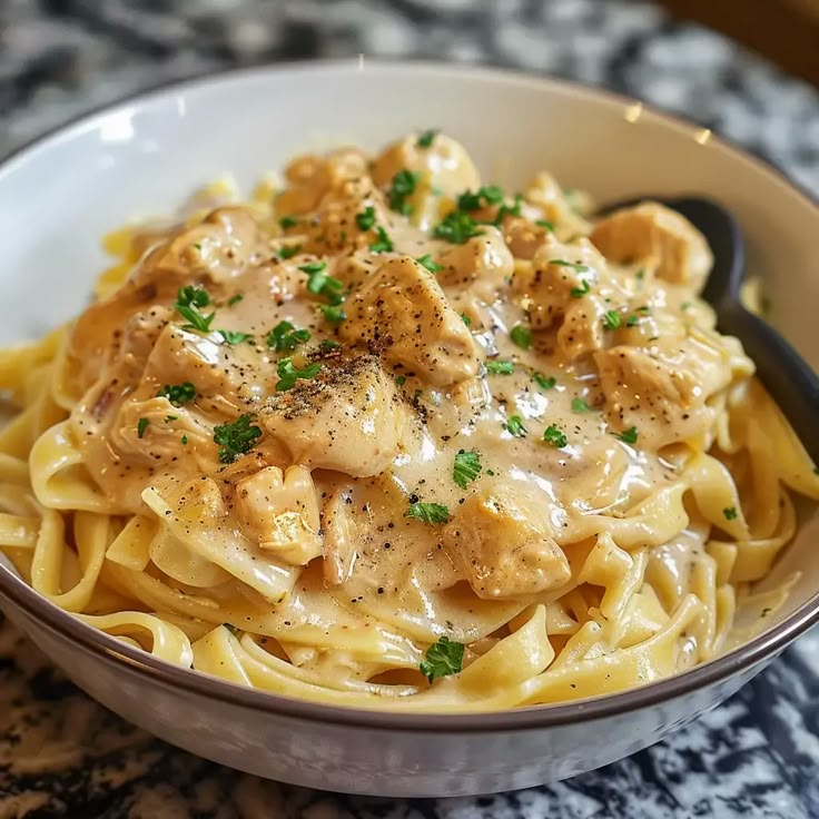 a white bowl filled with pasta covered in sauce and chicken meat on top of grated parmesan cheese