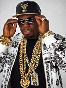 a man in a black hat and sunglasses holding his hands to his ears while wearing some gold chains