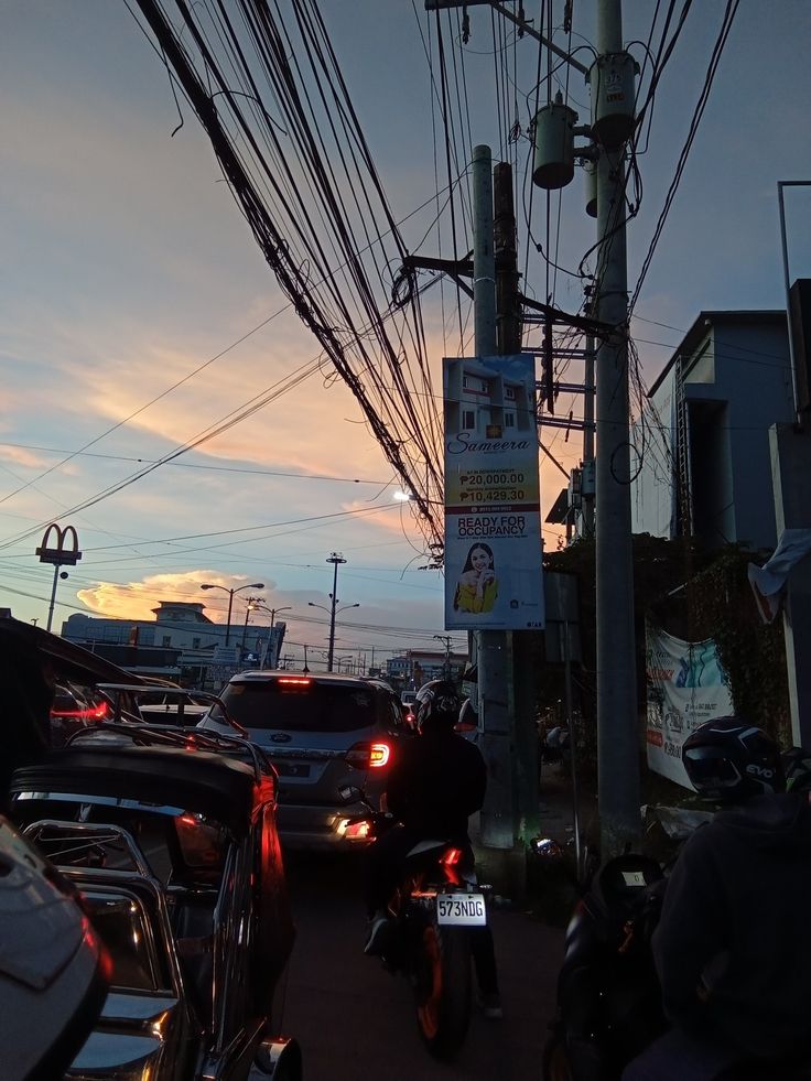 cars and motorbikes are parked on the side of the road near power lines