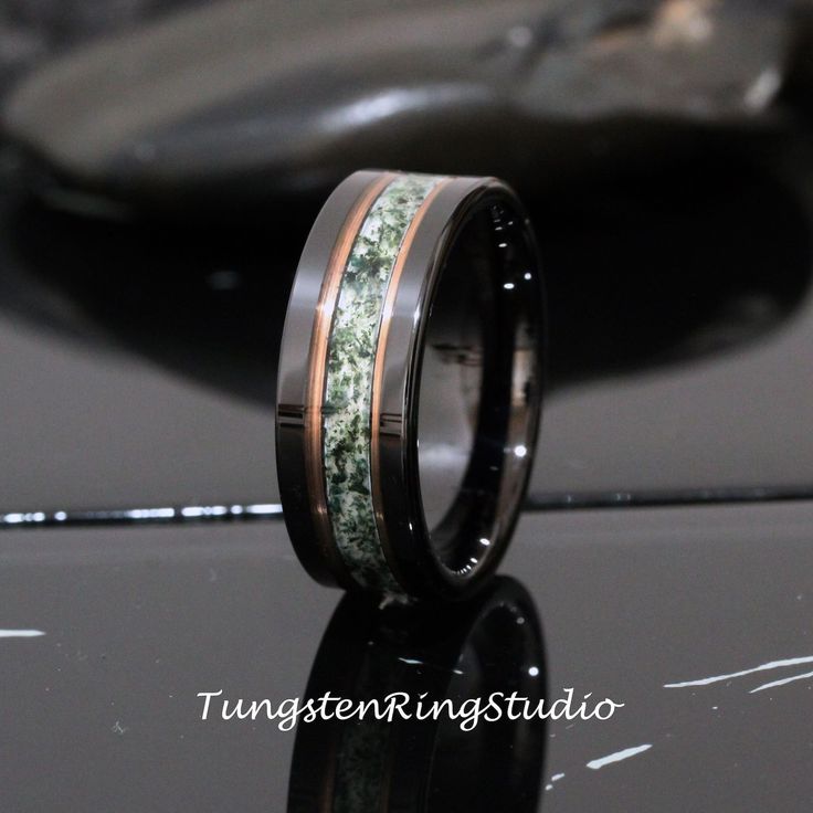 a wedding band with green moss inlays is shown on top of a black surface