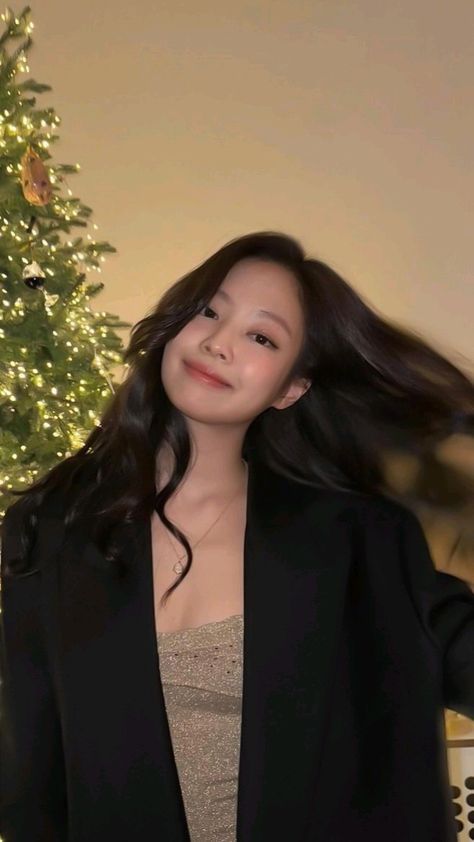 a woman standing in front of a christmas tree with her hair blowing in the wind