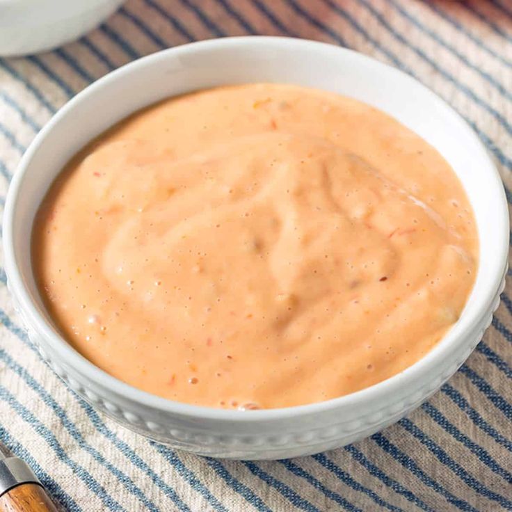 a white bowl filled with sauce sitting on top of a blue and white table cloth