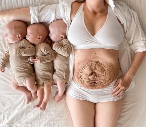 a woman laying on top of a bed next to three babys wearing diapers