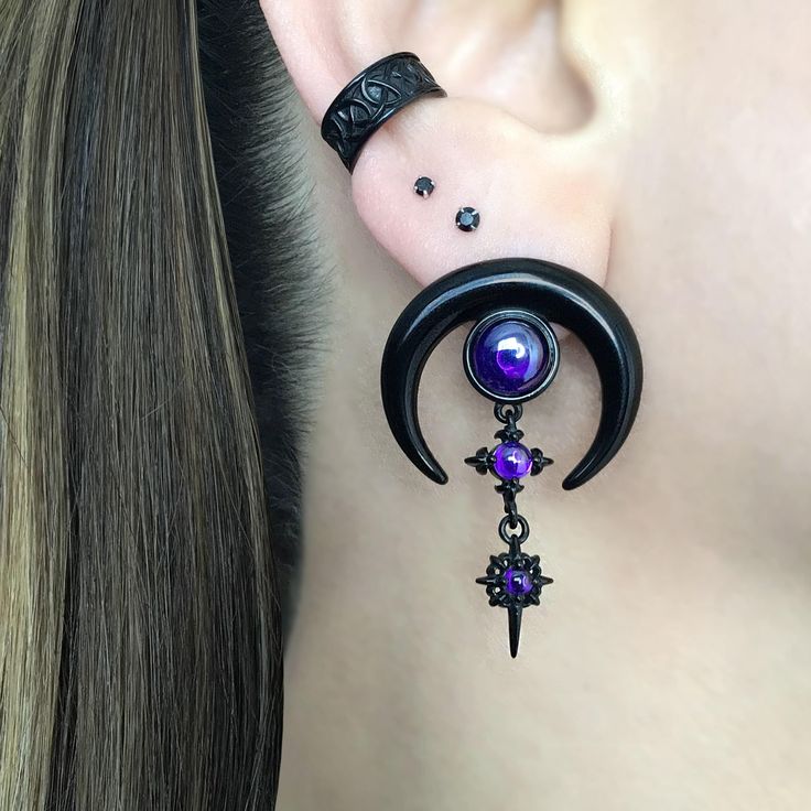 a woman wearing ear piercings with purple stones and black metal chains on her ears