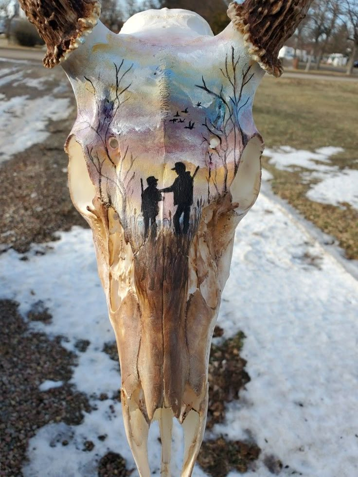 an animal skull with two people standing on it's side in front of snow covered ground