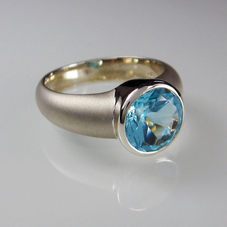 This Artemis Ring is made from brushed Sterling Silver and set with a genuine, natural 10 mm sky blue Topaz. Hallmarked in London UK Topaz Topaz is a silicate mineral of aluminium and fluorine and is found in a variety of colours such as blue, brown, orange, yellow green and fuschia (reddish pink). It's hardness is 8 on the Mohs hardness scale. Sometimes the material is treated in order to enhance the color. The name may be derived from the Sanskrit word "tapas" meaning heat or fire. It is said Modern Blue Topaz Round Ring, Modern Blue Topaz Ring, Round Shape, Modern Round Blue Topaz Ring, Modern Topaz Anniversary Ring, Modern Round Topaz Ring With Bezel Setting, Modern Blue Topaz Ring For Wedding, Modern Blue Topaz Wedding Ring, Modern Blue Topaz Ring With Tension Setting, Modern Blue Topaz Ring