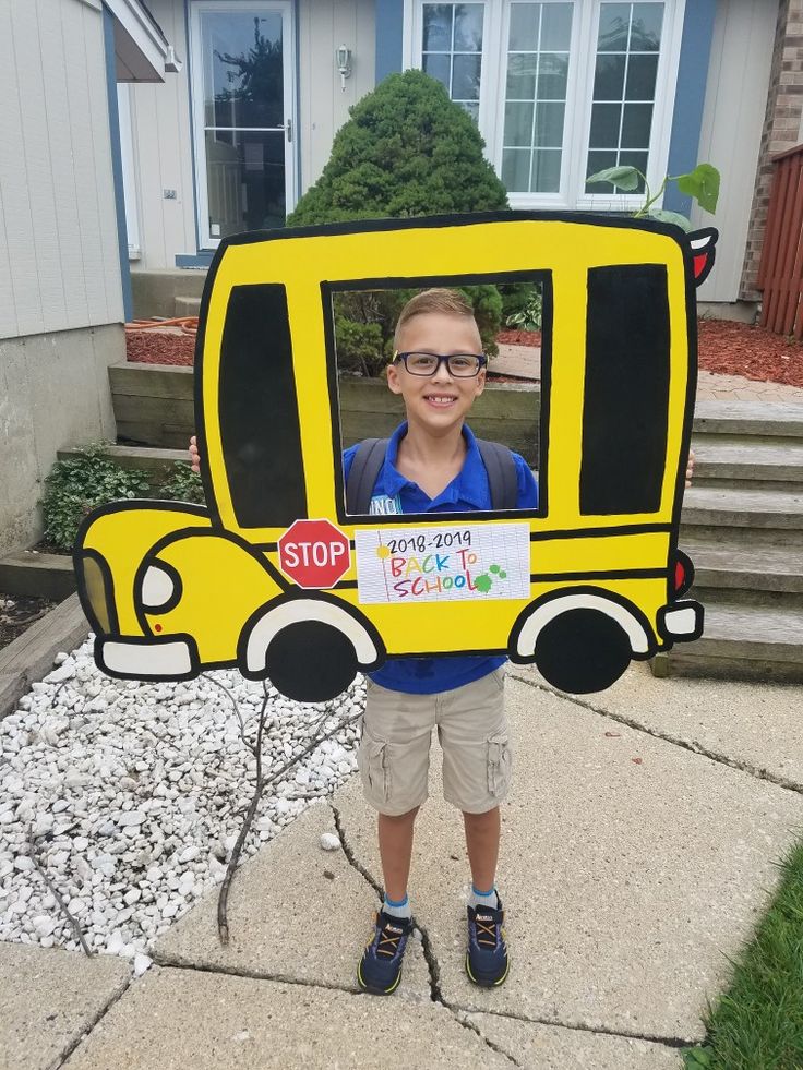 a young boy wearing glasses and holding up a cardboard school bus cutout in front of his face