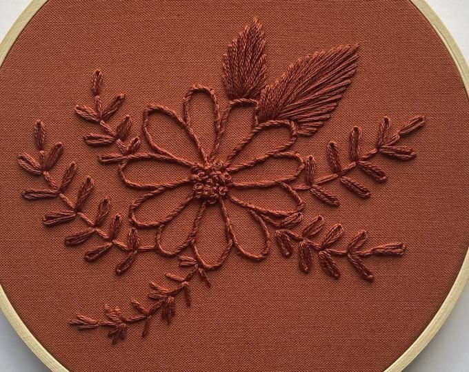 an embroidery pattern on a red cloth with leaves and branches in the center is shown