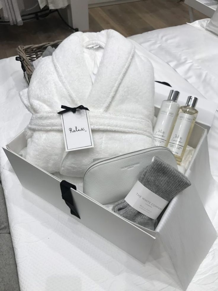 a bathrobe and toiletries are sitting in a box on a bed with white sheets