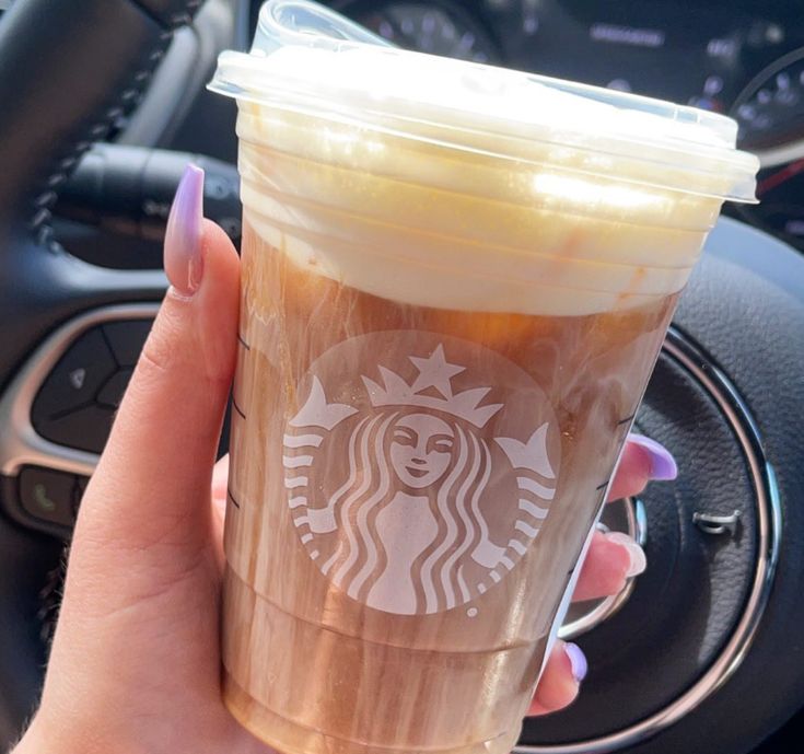 a woman holding up a cup of coffee in her hand with the steering wheel behind her