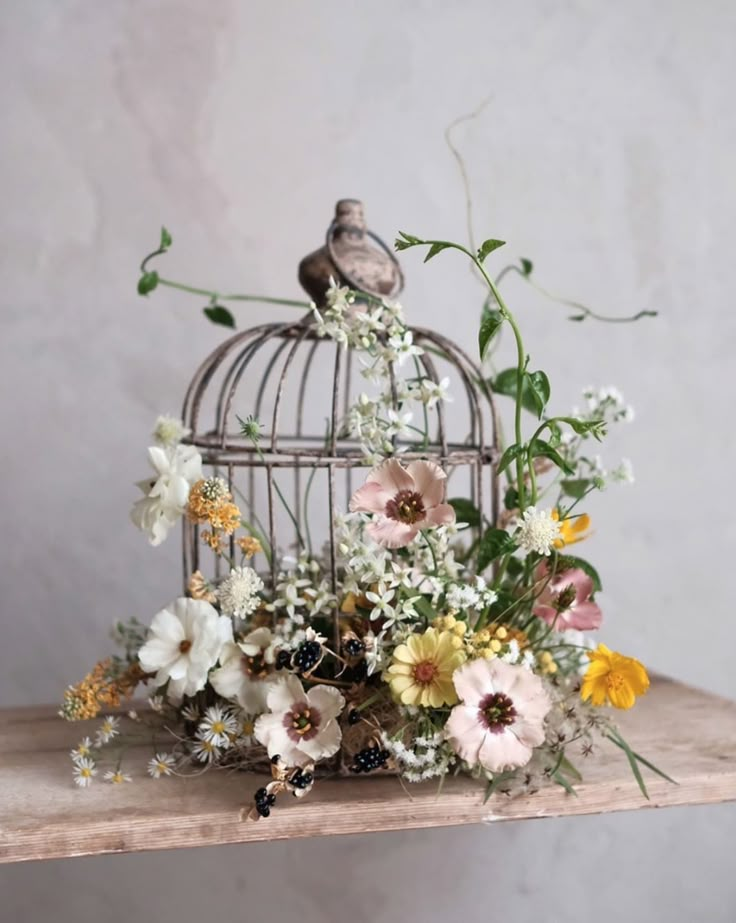 a bird cage with flowers in it sitting on a table