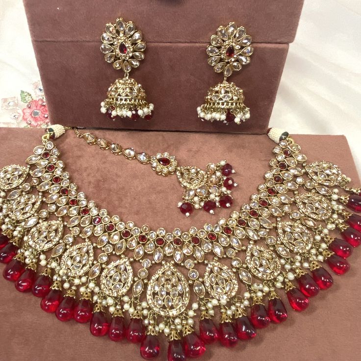 Beautiful antique gold necklace set with dazzling champagne zircon crystals and maroon stones. Plus maroon glass beads. Perfect bridal set Comes with matching jhumka earrings and matching tikka! Necklace 3 inch with adjustable string Earrings 2.25 Inch including jhumka length x 1 inch width Tikka 2.5 inch pendant plus 2 inch chain and 2 inch extender chain  Ready to be shipped ❤️ Ruby Jeweled Bridal Necklace For Wedding, Gold Crystal Bridal Necklace For Celebrations, Festive Crystal Jewelry With Stone Work, Wedding Kundan Necklace With Temple Jewelry Style, Festive Kundan Bridal Necklace With Stones, Wedding Temple Jewelry Kundan Necklace With Stones, Gold Bollywood Bridal Necklace With Stone Setting, Bollywood Style Gold Bridal Necklace With Stone Setting, Traditional Crystal Jewelry With Stone Work