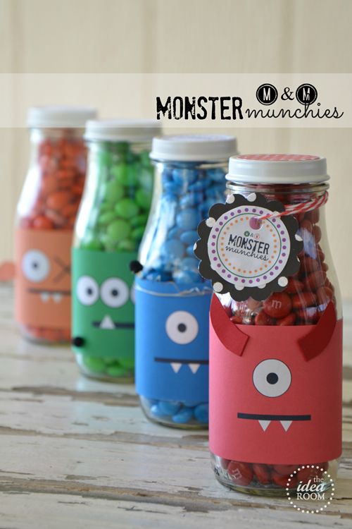 four jars with different colored candies in the shape of monster faces and eyes, on top of a wooden table