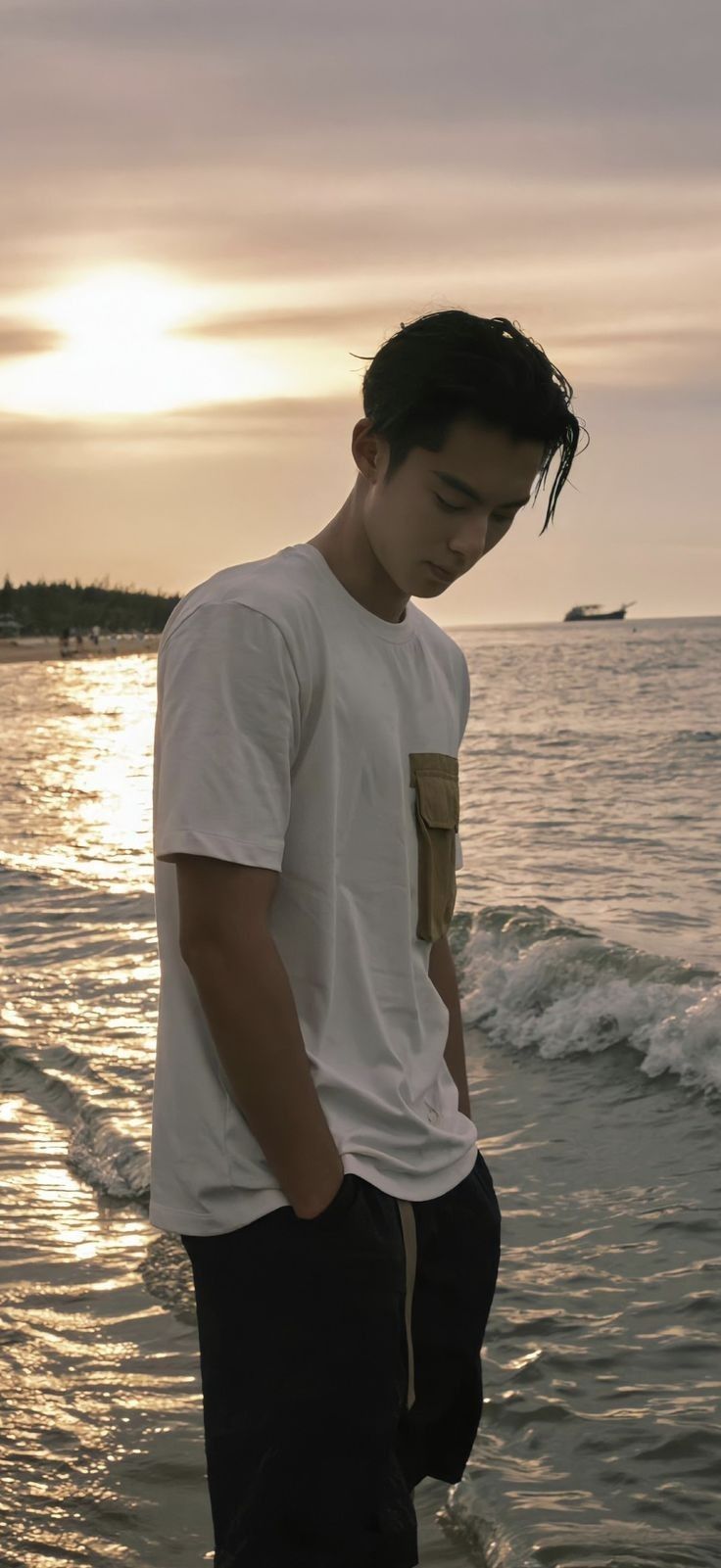 a young man standing on the beach at sunset