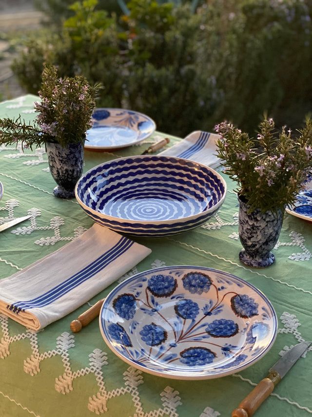 a table set with blue and white plates, napkins and flowers in vases