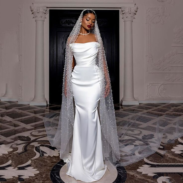 a woman in a white wedding gown and veil standing on the floor with her hands behind her back