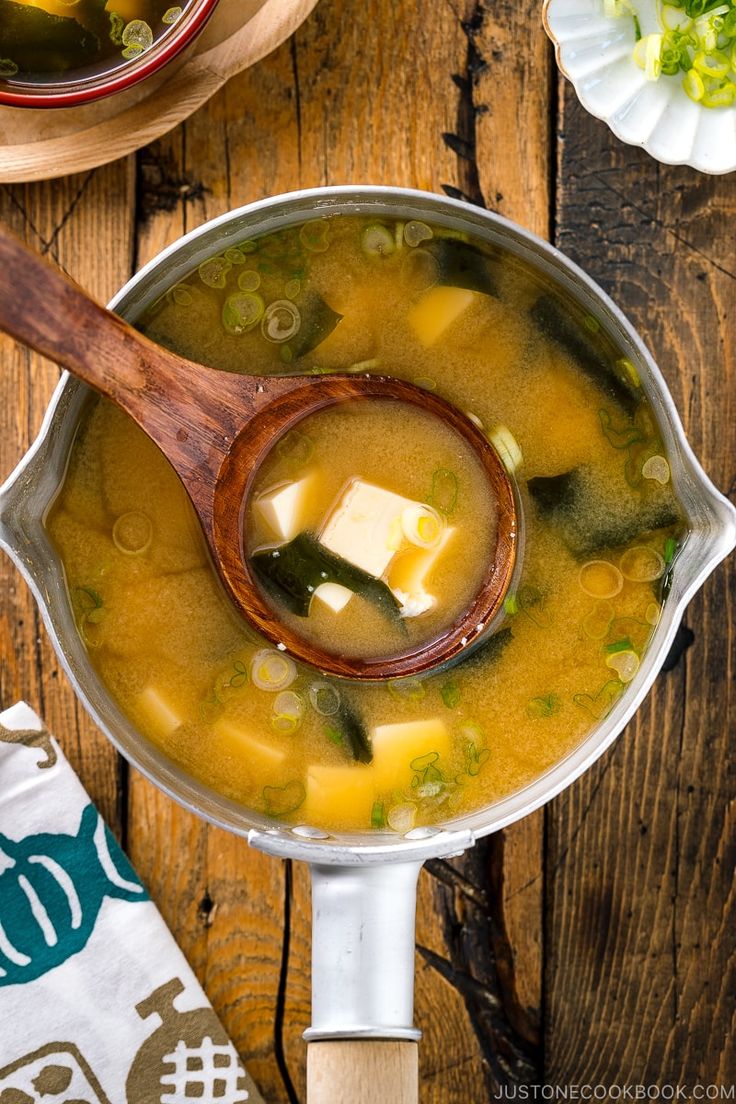 a wooden spoon in a pot filled with soup on top of a table next to other bowls