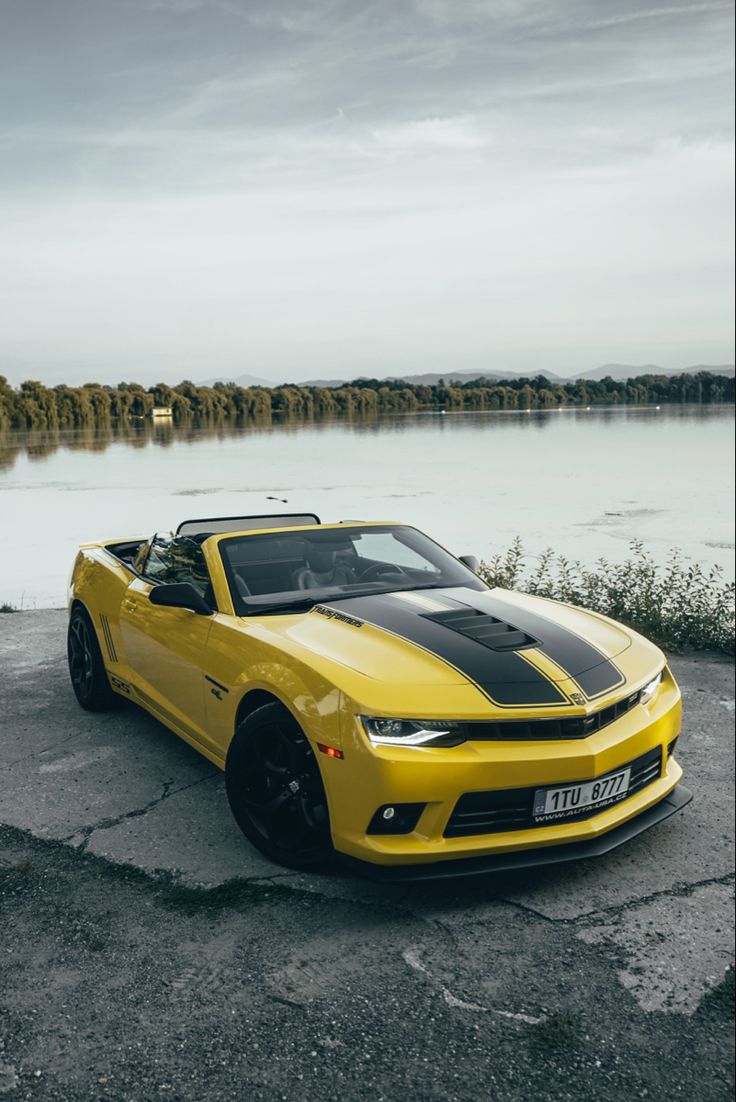 a yellow chevrolet camaro parked in front of a body of water on a cloudy day