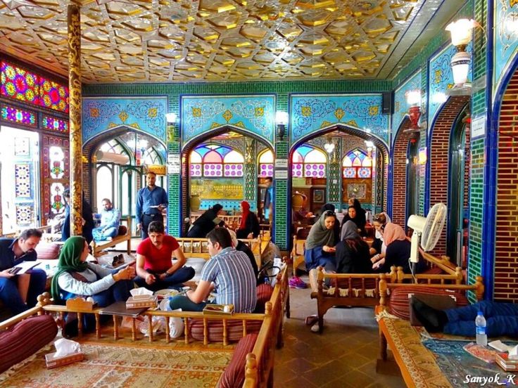 many people are sitting and standing in a room with stained glass windows on the ceiling