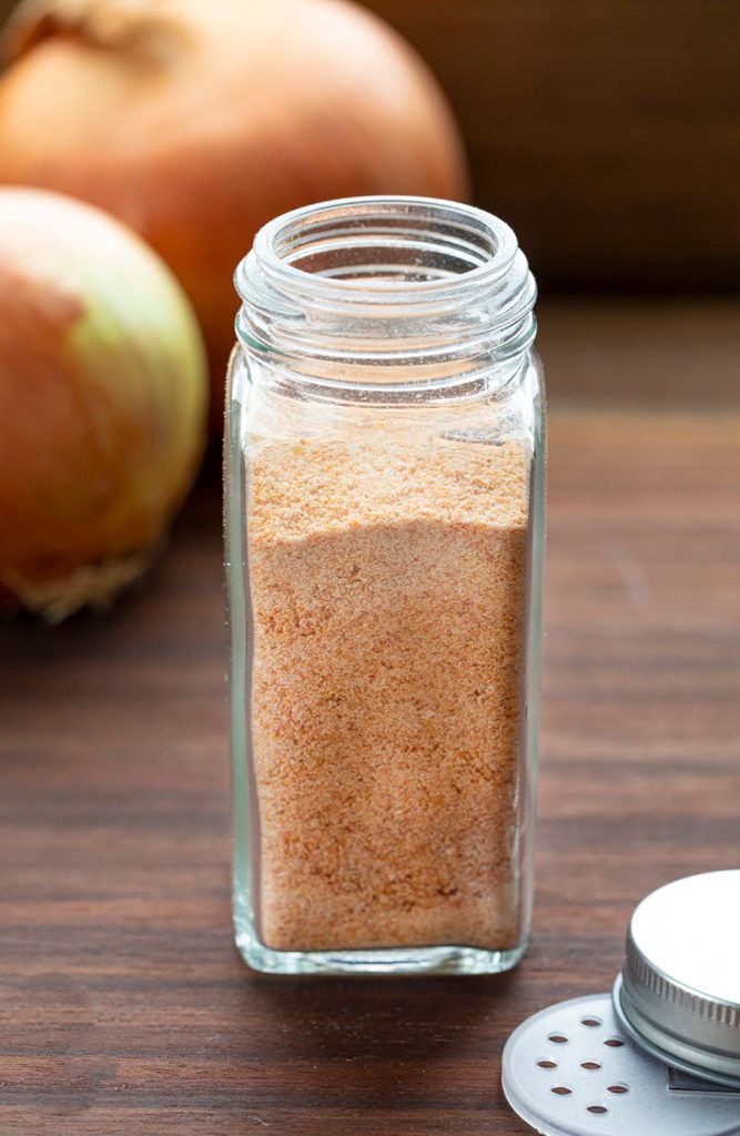 a glass jar filled with sand next to an onion and garlic grinder on a wooden table