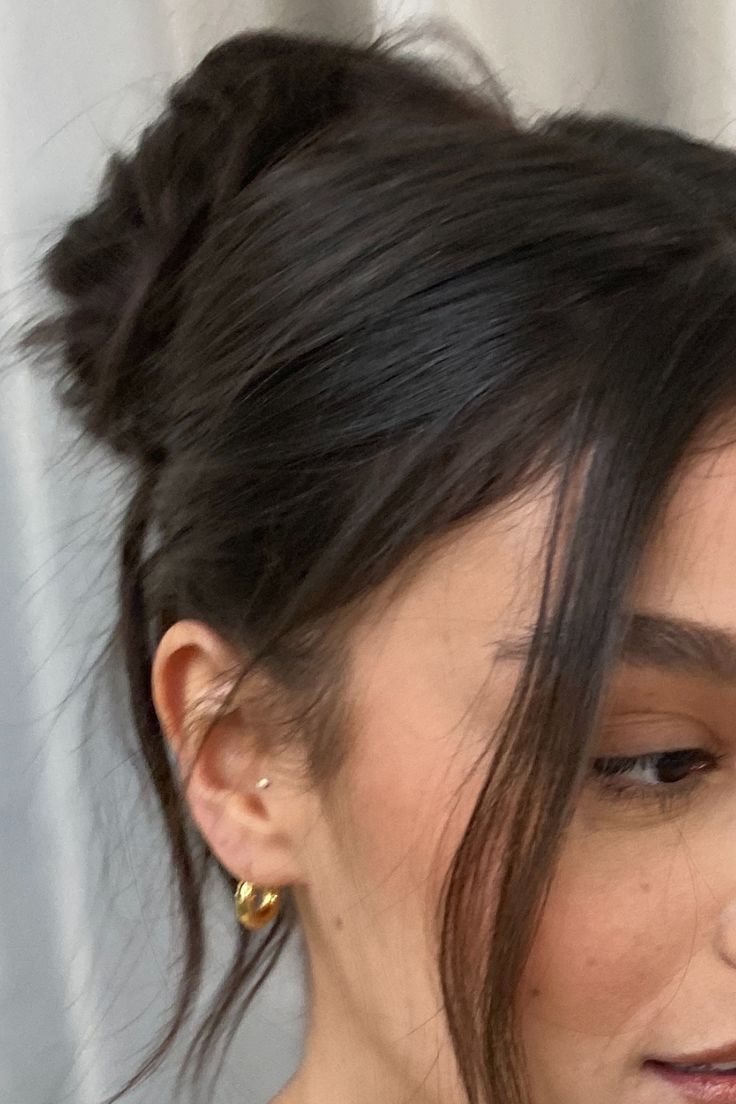 a close up of a person wearing gold earrings and a white shirt with black hair