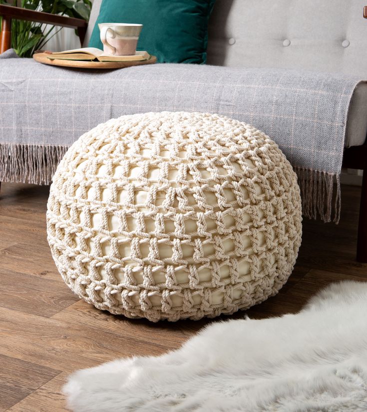 a white crocheted poufce sits on the floor in front of a couch