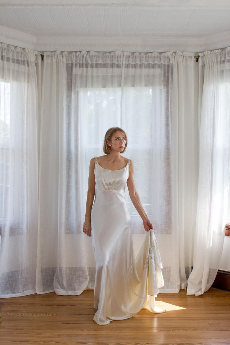 a woman in a white dress is standing by the window