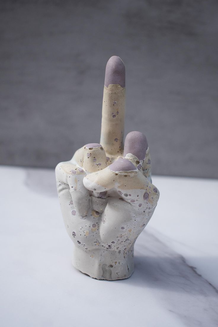 a ceramic hand with two fingers sticking out of it's middle and holding something up in the air