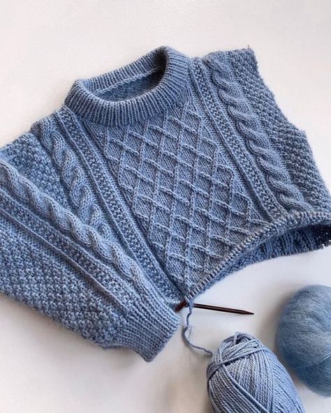 a blue knitted sweater and ball of yarn on a white surface with knitting needles