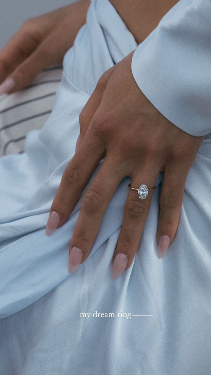 a woman's hand with a diamond ring on her left hand, sitting in a white dress