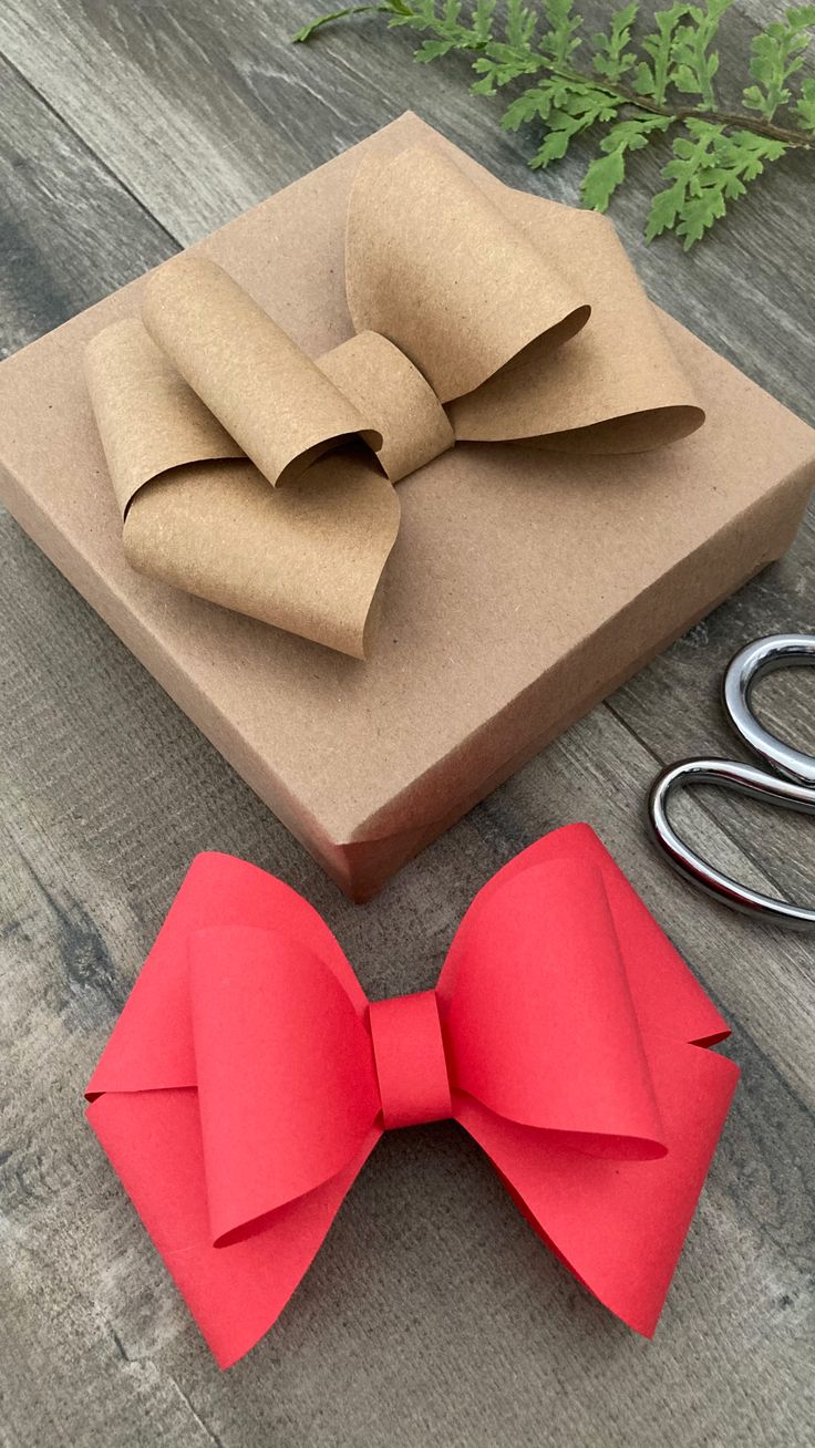 a red bow tie sitting on top of a wooden table next to scissors and a box