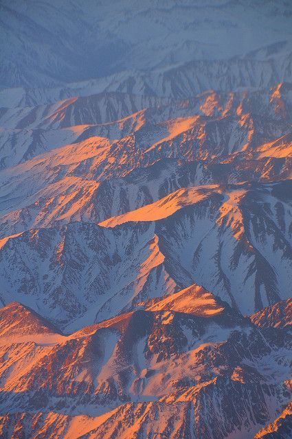 the view from an airplane window shows snow covered mountains and orange light in the sky